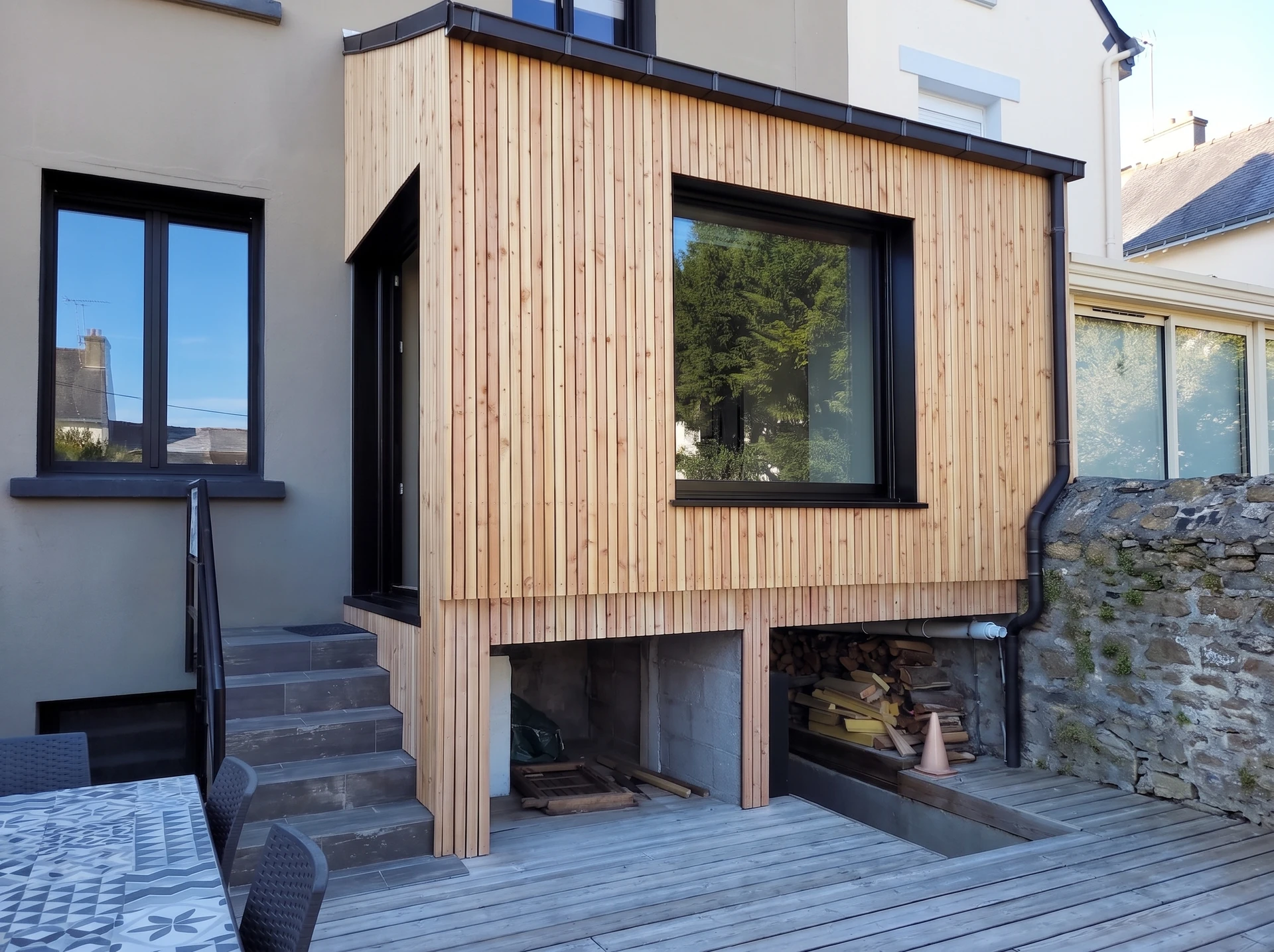 Extension de maison à ossature bois, bardage composite horizontal gris clair, toit plat avec gouttière métallique zinc